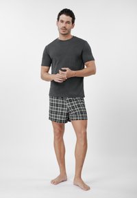 Vyriškas miego drabužių rinkinys: pilkas trumpomis rankovėmis marškinėlis su apvalia kaklo iškirpte; juodi ir balti languoti šortai; medvilnės mišinio medžiaga; laisvas kirpimas; minimalistinis dizainas.