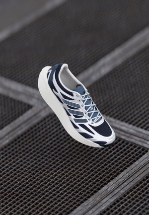 Chaussure de course avec des détails blancs, bleu marine et bleu clair flottant au-dessus d'une grille métallique.