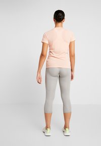 Vaaleanpunainen lyhythihainen t-paita, joka on yhdistetty harmaisiin, vartalonmyötäisiin capri-leggingseihin. Yläosassa on sileä tekstuuri ja leggingsissä on saumurivistettä.