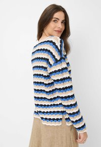 Strickpullover mit horizontalem Wellenmuster in Beige, Blau und Schwarz. Lange Ärmel, runder Halsausschnitt und seitliche Schlitze am Saum.