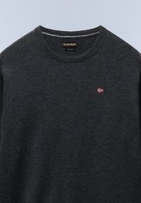 Pull en laine gris foncé tricoté avec un col rond et un petit détail de drapeau brodé rouge et blanc sur le côté gauche de la poitrine.