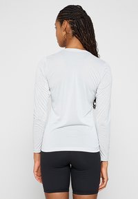 Jasnoszara, długorękawowa koszulka sportowa z teksturowanej tkaniny, z okrągłym dekoltem i kontrastowymi szwami, połączona z czarnymi dopasowanymi szortami.