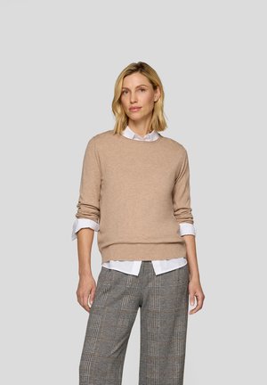 Beige gestrickter Pullover mit Rundhalsausschnitt, langen Ärmeln und geripptem Saum, über einem weißen Hemd mit Kragen getragen. Karierte Hosen sind sichtbar.