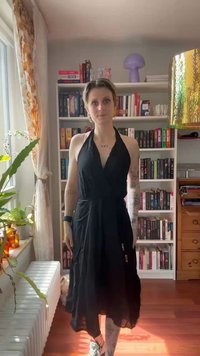 Svart halterneck-kjole, lett stoff, flytende fasong, lengde til midten av leggen, med innsnørt midje. Brukt med flerfarget joggesko.