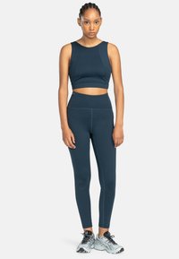 Marineblauw sportset, bestaande uit een cropped top met brede banden en hoge taille leggings. Glad oppervlak, aansluitend ontwerp met nette naden.
