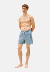 Bañador azul claro con cintura elástica y cordón, que presenta un logo azul oscuro impreso en un lateral. Textura suave, largo hasta la rodilla.