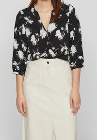 Blusa nera con fantasia floreale bianca, scollatura a V e maniche a tre quarti. Abbinata a pantaloni chiari con tasche frontali.