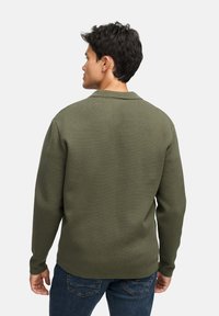 Olivgrön tröja med strukturerad stickning, långa ärmar, krage och avslappnad passform, ihop med mörka jeans.