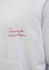 Sweatshirt gris clair avec une texture douce, doté d'une poche avant et d'une broderie détaillée en maroon qui lit "Originals Worldwide Atelier."