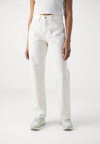 White high-waisted jeans made of denim, featuring a straight leg design, subtle fading, and stitched detailing; worn with light gray sneakers.