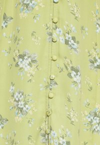 Tissu vert clair avec de petits motifs floraux bleus et blancs, présentant une rangée verticale de boutons recouverts au centre.