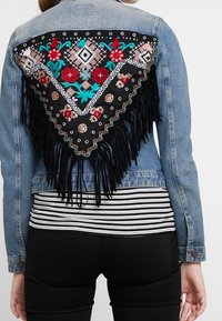 Jeansjacka med en svart broderad rygg med blommiga och geometriska mönster, prydd med pärldetaljer och lång svart frans.