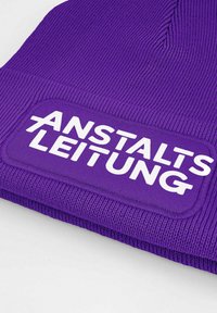 Purple knitted beanie with ribbed texture featuring a rectangular patch that reads "ANSTALTSLEITUNG" in bold white letters.