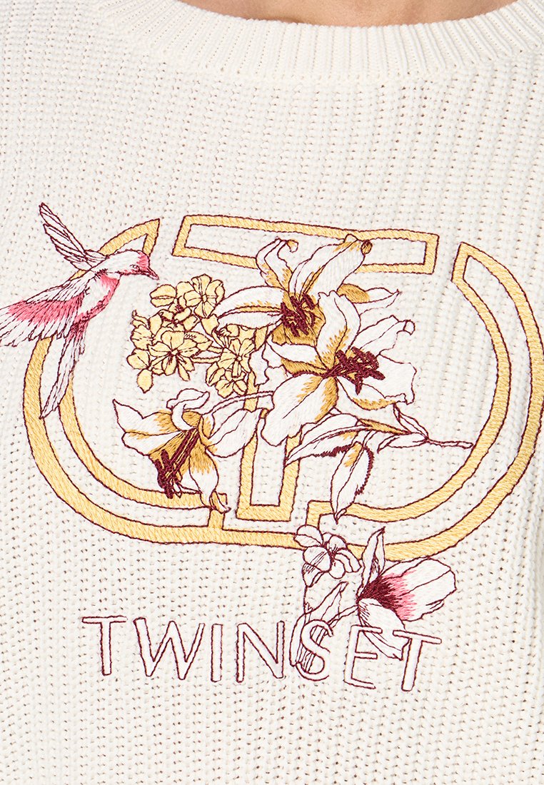 Witte gebreide trui met meerkleurige bloemenborduursels, een kolibrie en de merknaam "TWINESET" in decoratieve stiksels.