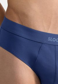 Himmelblaue Baumwollslips mit glatter Textur, elastischem Bund mit "SLOG"-Branding und tailliertem Design.