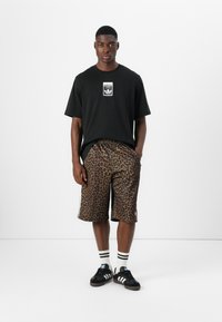 Black t-shirt with a white logo, brown leopard print shorts, black sneakers with white stripes, and black-and-white striped socks.
