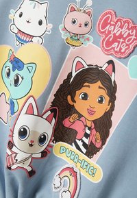 Gaiši zils džemperis ar krāsainiem multfilmu varoņiem, tostarp kaķiem un meiteni, ar grafisku tekstu "PURR-IFIC!" un varavīksnes akcentiem.