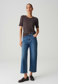 Dark gray short-sleeve ribbed t-shirt, high-waisted blue wide-leg jeans, and black loafers on a neutral background.