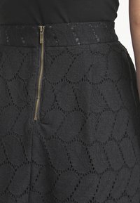 Zwarte rok gemaakt van een textuurstof met een bladerenpatroon, een zichtbare gouden ritssluiting aan de achterkant en een aansluitend taillebandontwerp.