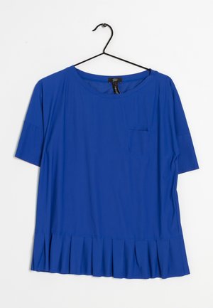 Blouse bleue à manches courtes avec encolure ronde et petite poche poitrine, suspendue sur un cintre noir sur fond blanc.