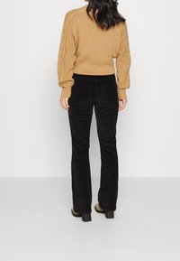 Burgundy kabelstickad tröja med ballongärmar, i kombination med svarta kordfläksbyxor med utsvängd ben. Modellen visas bakifrån.