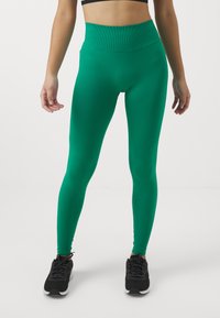 Green high-waisted leggings with a smooth texture, fitted design, and a stretchy waistband. Paired with black athletic shoes.