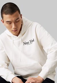 Biała bluza z kapturem z haftem "Nowy Jork" i "Calvin Klein Jeans" w kolorze czarnym. Wykonana z miękkiego materiału, z prążkowanymi mankietami i kieszenią z przodu.
