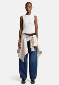 Biały prążkowany tank top w połączeniu z luźnymi, niebieskimi dżinsami. Jasnobeżowa koszula związana w pasie, do tego ciemny pasek i czarne buty.