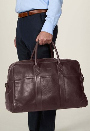Læder rejsetaske i dyb burgundy, med dobbelt top-håndtag, stikninger og en glat tekstureret overflade.