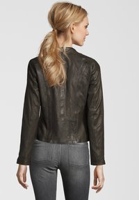 Dunkelgrüne Lederjacke mit taillierter Passform, langen Ärmeln und Nahtdetails. Über grauen Denim-Jeans getragen, von hinten gesehen.