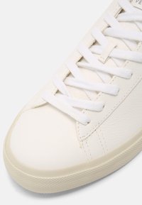 Hvit lær sneakers med hvite flate snorer, teksturert overdel, rund tå og gummisåle med diamantmønster.