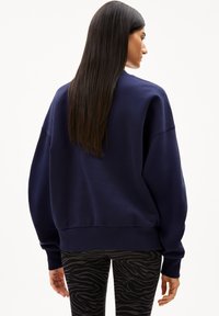 Navy blue sweatshirt with a relaxed fit, dropped shoulders, and ribbed hem. Paired with black and gray zebra-patterned leggings.