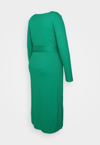 Vestido longo maxi verde de lã com mangas longas, uma silhueta ajustada e um cinto na cintura. Apresenta fendas laterais para maior movimento.