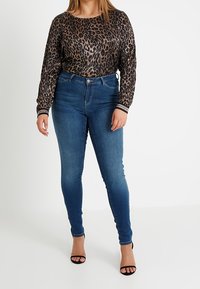 Suéter de leopardo con mangas largas, combinado con jeans ajustados azules. El conjunto presenta una cintura alta y tacones negros con tiras.