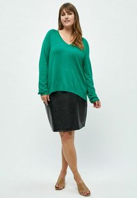Maglione verde a collo a V con maniche lunghe, abbinato a una gonna a matita nera in ecopelle e sandali beige.