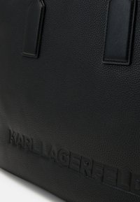 Sorte tekstureret læderhåndtaske med et debosseret logo, der har to top håndtag og en rektangulær form for praktisk brug.