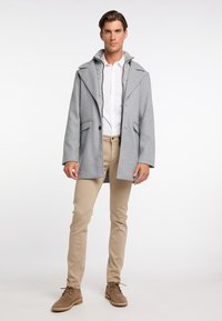 Grå uldblanding frakke med krave, store klapper og to frontlommer. Båret over en hvid skjorte og beige slim-fit bukser.