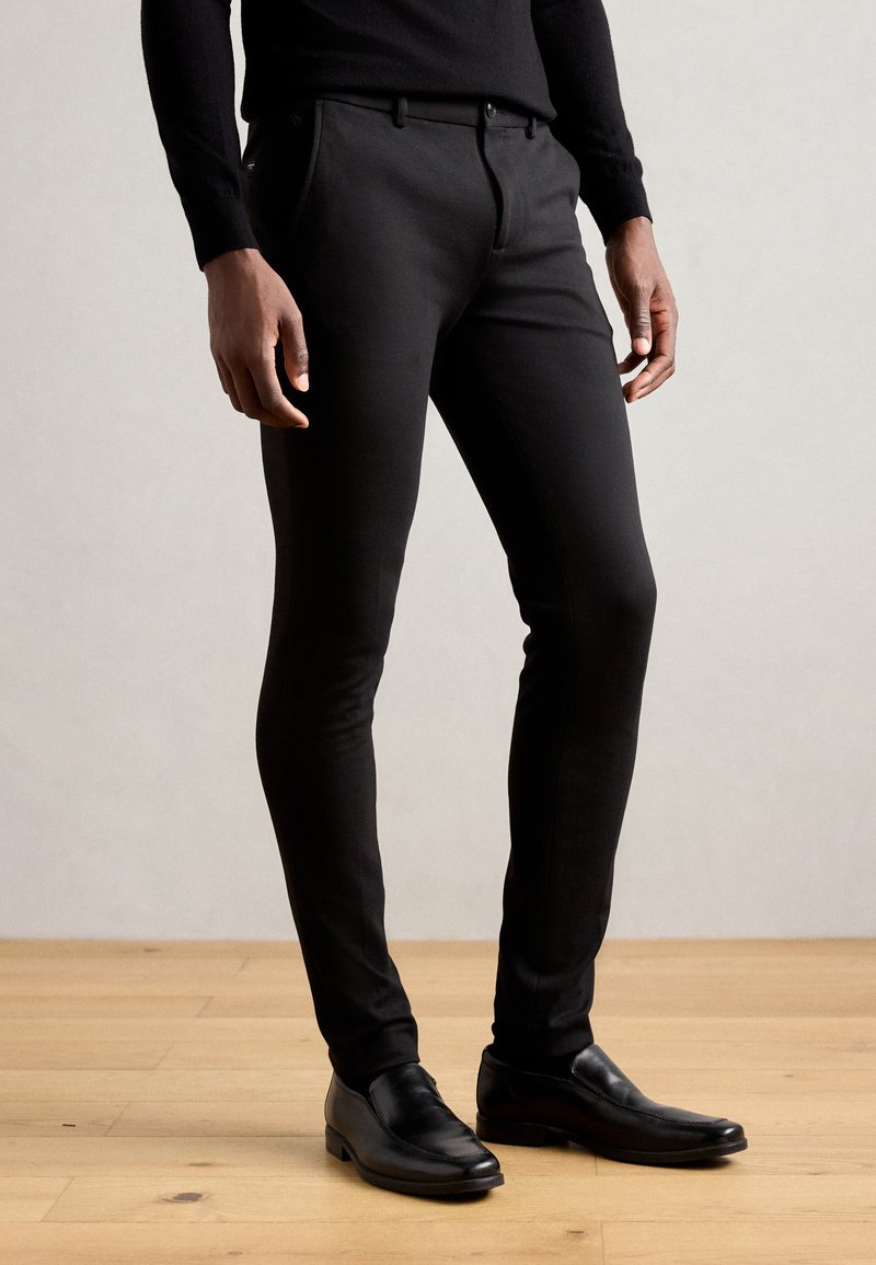 Zwarte slim-fit broek gemaakt van een gladde, rekbare stof, met een platte voorkant, zijzakken en een strakke tailleband.