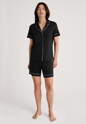 Zwart pyjama-set met korte mouwen bestaande uit een knoopsluiting shirt met witte bies en bijpassende shorts. Zachte stof, relaxed fit en zonder patronen.
