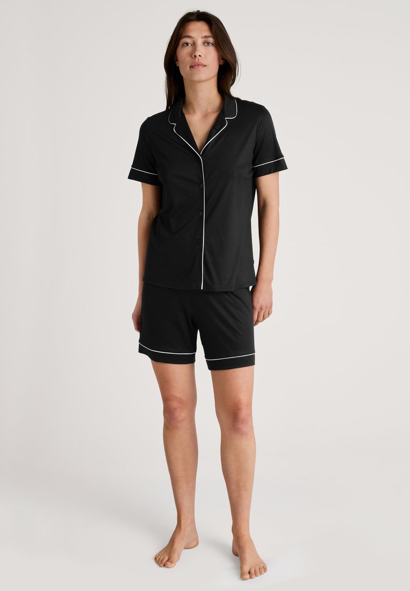 Zwart pyjama-set met korte mouwen bestaande uit een knoopsluiting shirt met witte bies en bijpassende shorts. Zachte stof, relaxed fit en zonder patronen.