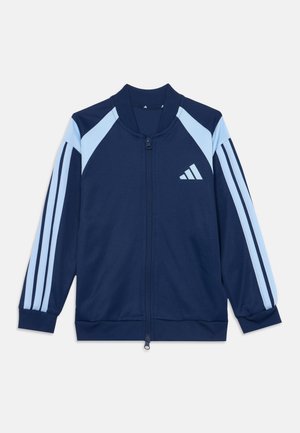 Veste de sport bleu marine à fermeture éclair avec des bandes bleu clair sur les manches et les panneaux d'épaule, avec un logo Adidas blanc sur la poitrine.