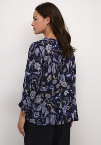Blusa blu navy con motivo paisley in tonalità di blu, bianco e oro. Presenta una vestibilità morbida con maniche a tre quarti e scollatura rotonda.