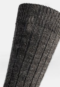 Calzino di lana grigio scuro con texture a coste verticali. Presenta una leggera trasparenza e un aspetto morbido e peloso.