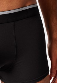 Black boxer shorts made of soft fabric with a plain design, featuring a contrasting gray waistband. Smooth texture and fitted shape.