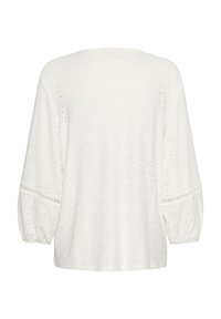 Blouse blanche en tissu texturé avec des motifs à pois, manches longues amples et col rond. Manches bouffantes aux poignets.