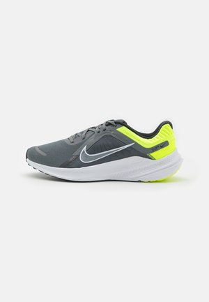 Szaro-neonowo-żółty but do biegania Nike z białą podeszwą i czarnym logo Swoosh, pokazany z boku na białym tle.
