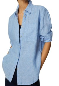 Camisa de botones de color azul claro hecha de una tela texturada. Cuenta con un bolsillo en el pecho y mangas enrolladas. Diseño simple con un ajuste relajado.