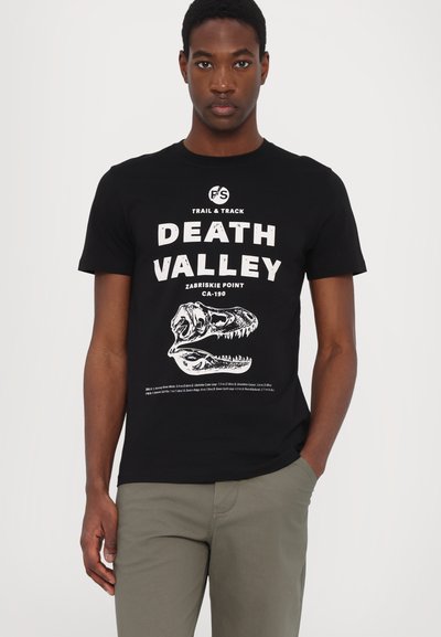 Czarna bawełniana koszulka z białym nadrukiem graficznym czaszki dinozaura oraz tekstem "DEATH VALLEY" z dodatkowymi szczegółami poniżej.