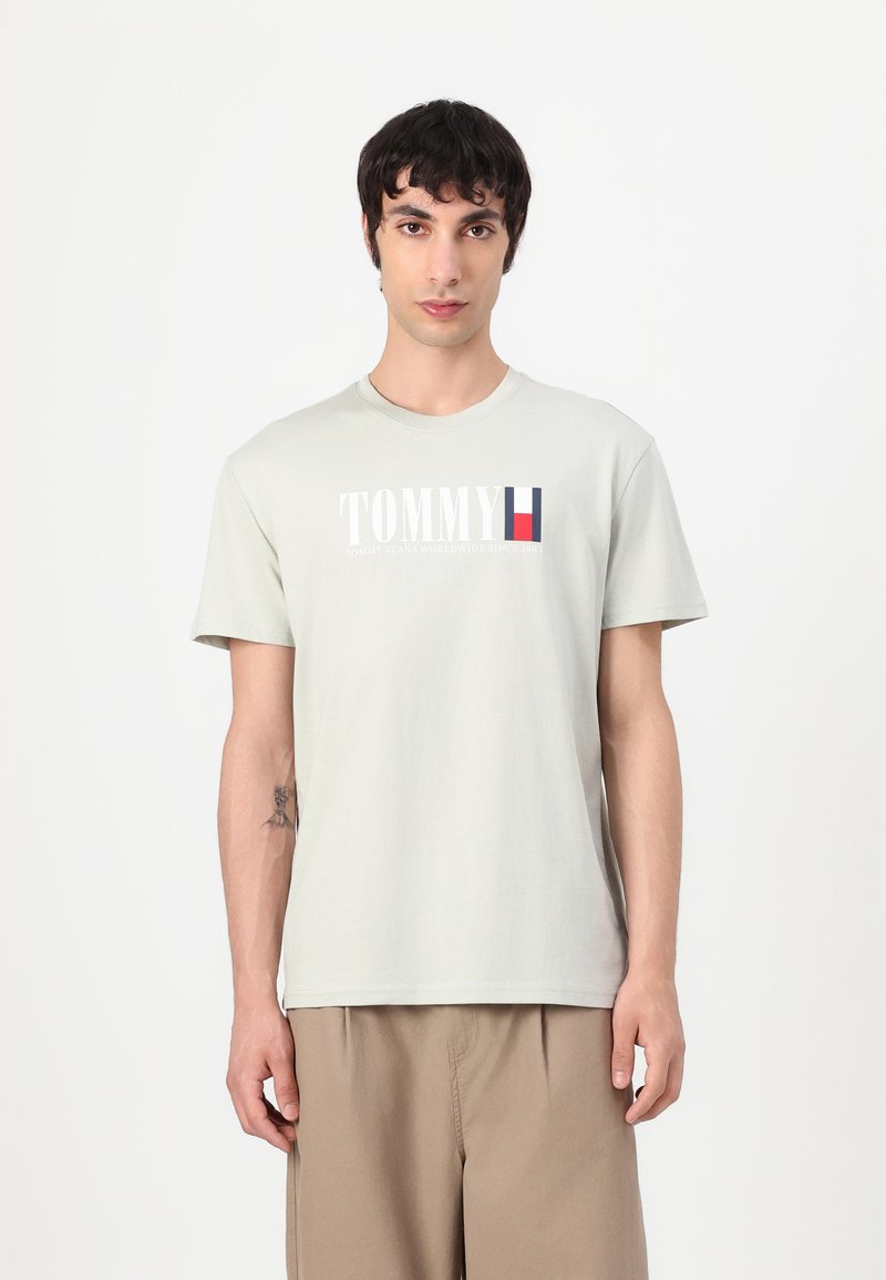 Light gray cotton t-shirt with short sleeves, round neckline, featuring "TOMMY" logo and striped accent in red, white, and blue.
