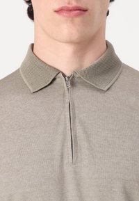 Polo shirt beige à fermeture éclair avec un col en maille texturée et un tissu lisse. Conception ajustée, détails de couture minimaux et sans motifs.